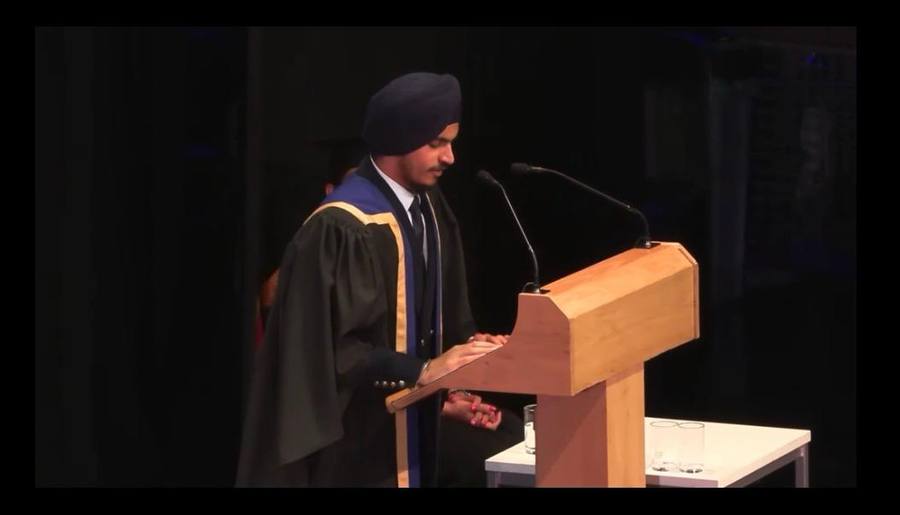 Eshwinder in graduation gown, addressing the audience from a podium at Queen Mary graduation