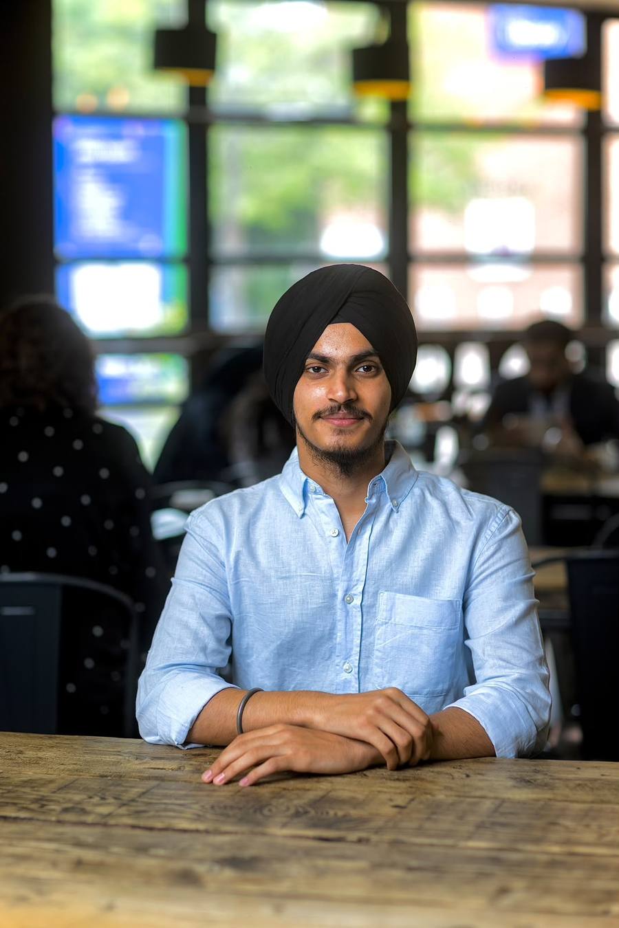 Eshwinder Singh, smiling, sitting at a wooden table in a café